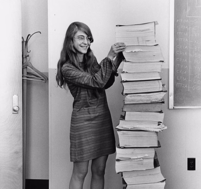 Margaret Hamilton debout à côté de la pile de code du programme Apollo